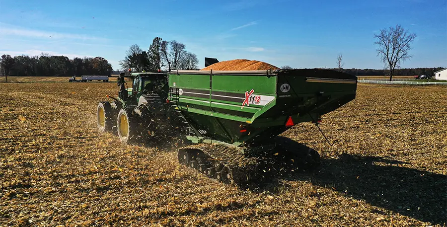 green 1112 grain cart with stx2 tracks driving through a corn field