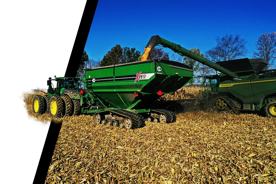 a green 1112 grain cart with stx2 tracks driving through a corn field receiving grain from a combine