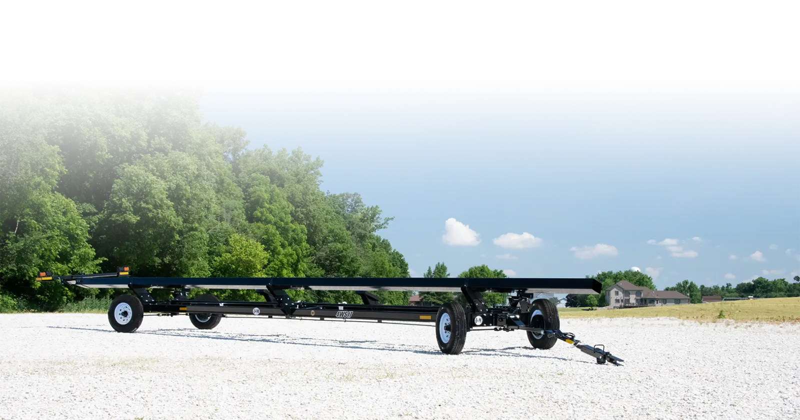 a 4-wheel steer header transport sitting in the lot in front of a field.